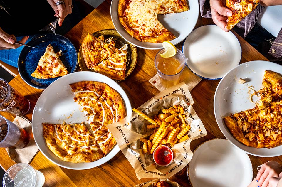 A table with crinkle cut fries, The Upstate and Lucky Lou Pizza served with refreshments