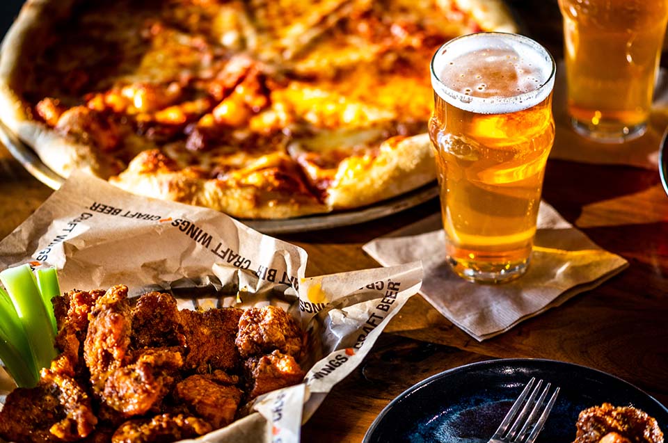 Wings served with a beer and a pizza in the background